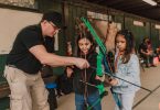 cute attentive diverse little girl practicing archery with male instructor