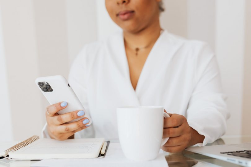 person in white top holding white ceramic mug while using cellphone