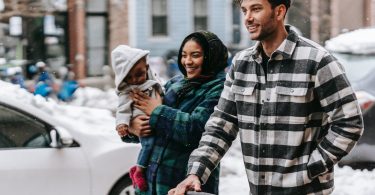 cheerful young diverse family with toddler strolling on street and smiling