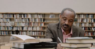 man in gray suit jacket sitting beside books