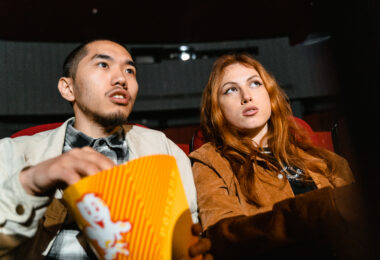 A woman sitting next to a man holding a popcorn box