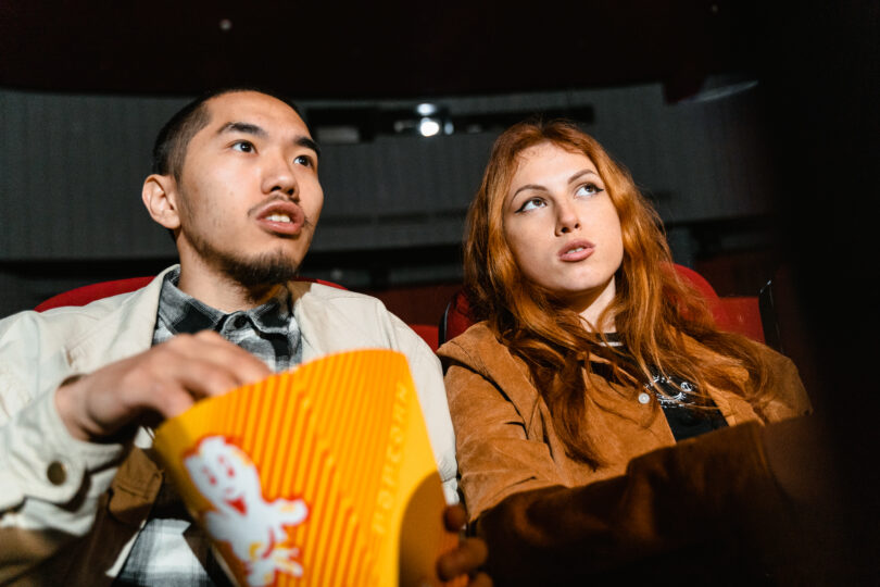 A woman sitting next to a man holding a popcorn box