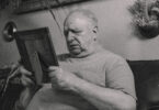 A grayscale photo of an elderly man holding a wooden frame