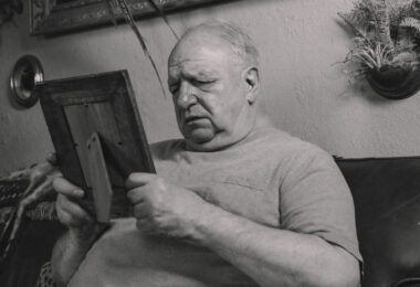A grayscale photo of an elderly man holding a wooden frame
