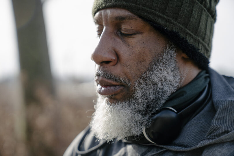 Serious bearded black man in warm clothes with closed eyes