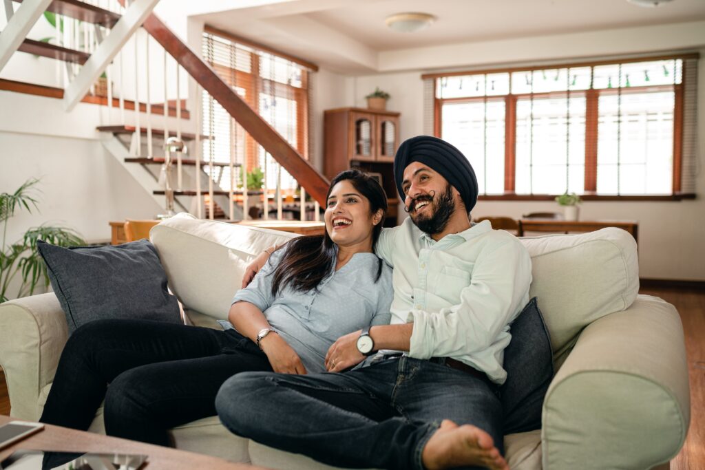 Joyful young indian couple cuddling while watching funny film on tv