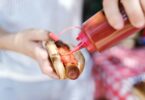 A person putting ketchup on the hot dog