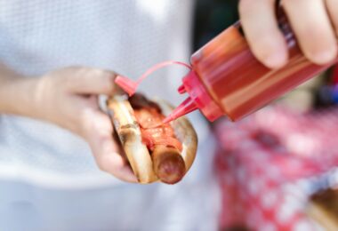 A person putting ketchup on the hot dog
