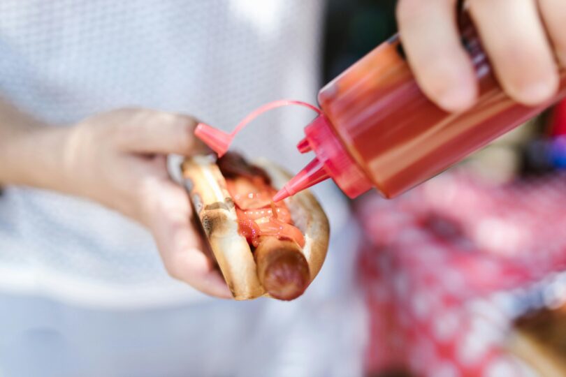 A person putting ketchup on the hot dog