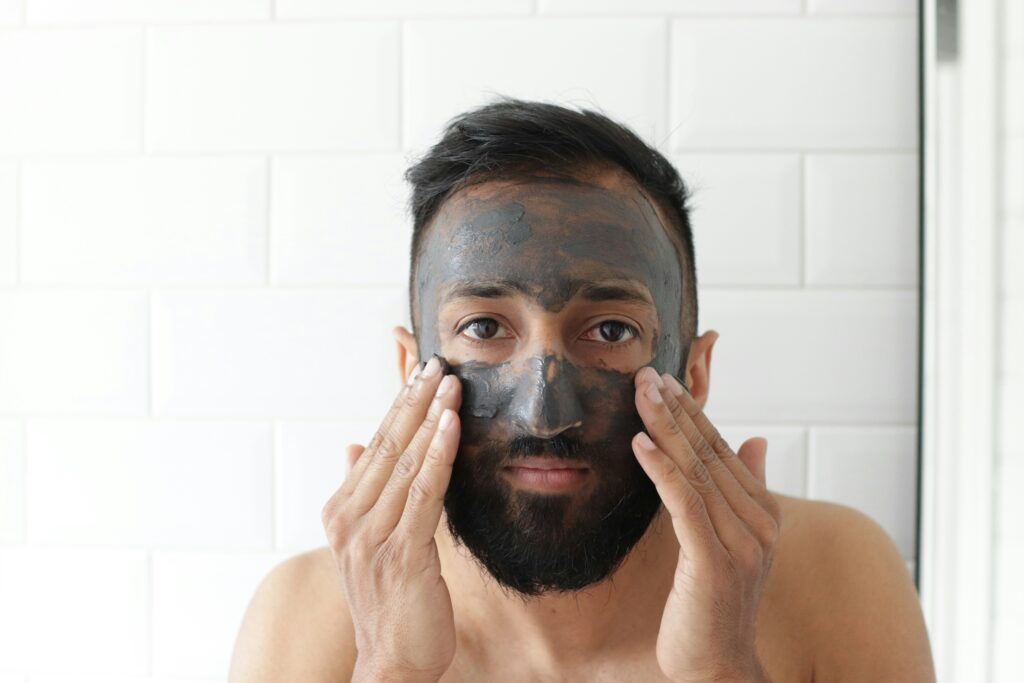 Indian man applying charcoal face mask. Self care.