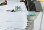 Laptop and pile of paper documents on white table